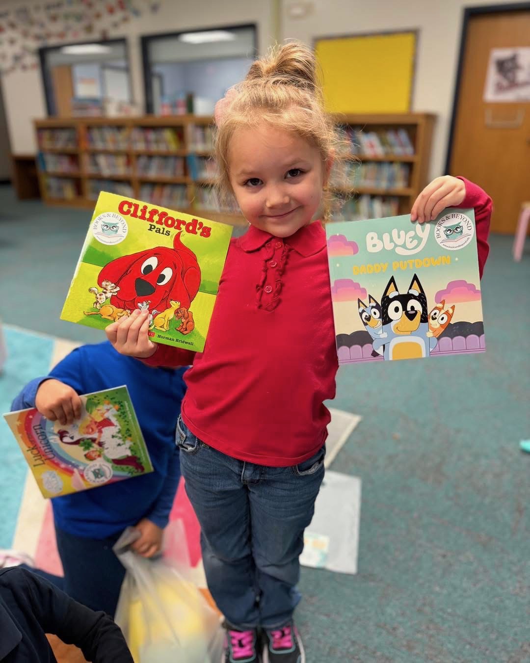 A young reader holding Clifford and Bluey books in a school library